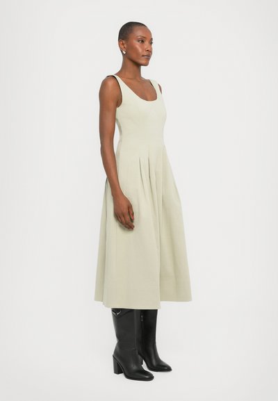 Light green sleeveless dress with a fitted bodice and pleated skirt, paired with black heeled boots. Smooth texture and classic silhouette.