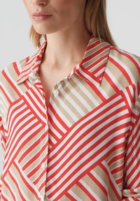 Camicia con colletto caratterizzata da strisce diagonali alternate rosse, beige e bianche. Realizzata in tessuto morbido con bottoni sulla parte anteriore.