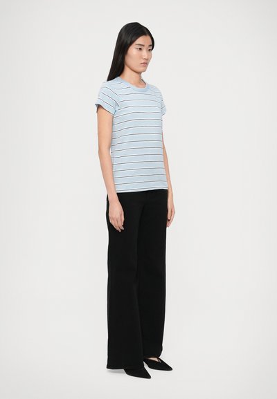 Svetlomodré tričko s pruhmi a založenými rukávmi, v kombinácii s čiernymi širokými nohavicami. Tričko má biele a tmavé pruhy pre kontrast.