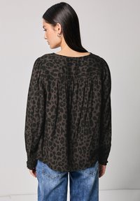 Černý top s leopardím potiskem, dlouhými rukávy s nabíranými manžetami a kulatým výstřihem. Vypadá jako vyrobený z lehkého materiálu.
