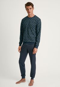Marineblauw pyjama set met een langwerpige, gestreepte top met groene accenten en bijpassende effen broek, gemaakt van zachte, lichte stof.