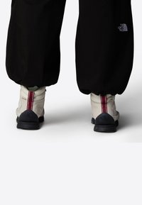 Bottes blanches et grises avec une rayure bordeaux, semelles noires et logo. Associées à un pantalon noir ample et fuselé.