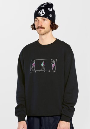Sweat-shirt noir avec un col ras du cou et des manches longues, arborant un design graphique coloré avec quatre personnages et le texte "VOLCOM" en bas.
