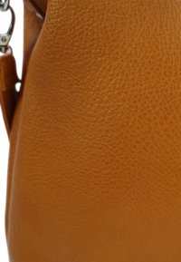 Bruine leren handtas met een gestructureerd oppervlak, ronde vorm en zilveren hardwareaccenten. Close-upweergave benadrukt de materiaaldetails.