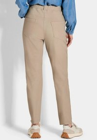 Beige rechte pantalon met een gladde textuur, voorzien van twee achterzakken, gecombineerd met beige en witte sneakers.