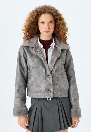Chaqueta corta de símil borreguillo gris con collar de pelo sintético, dos bolsillos frontales y cierre de dos botones. Presenta una textura suave y un corte holgado.