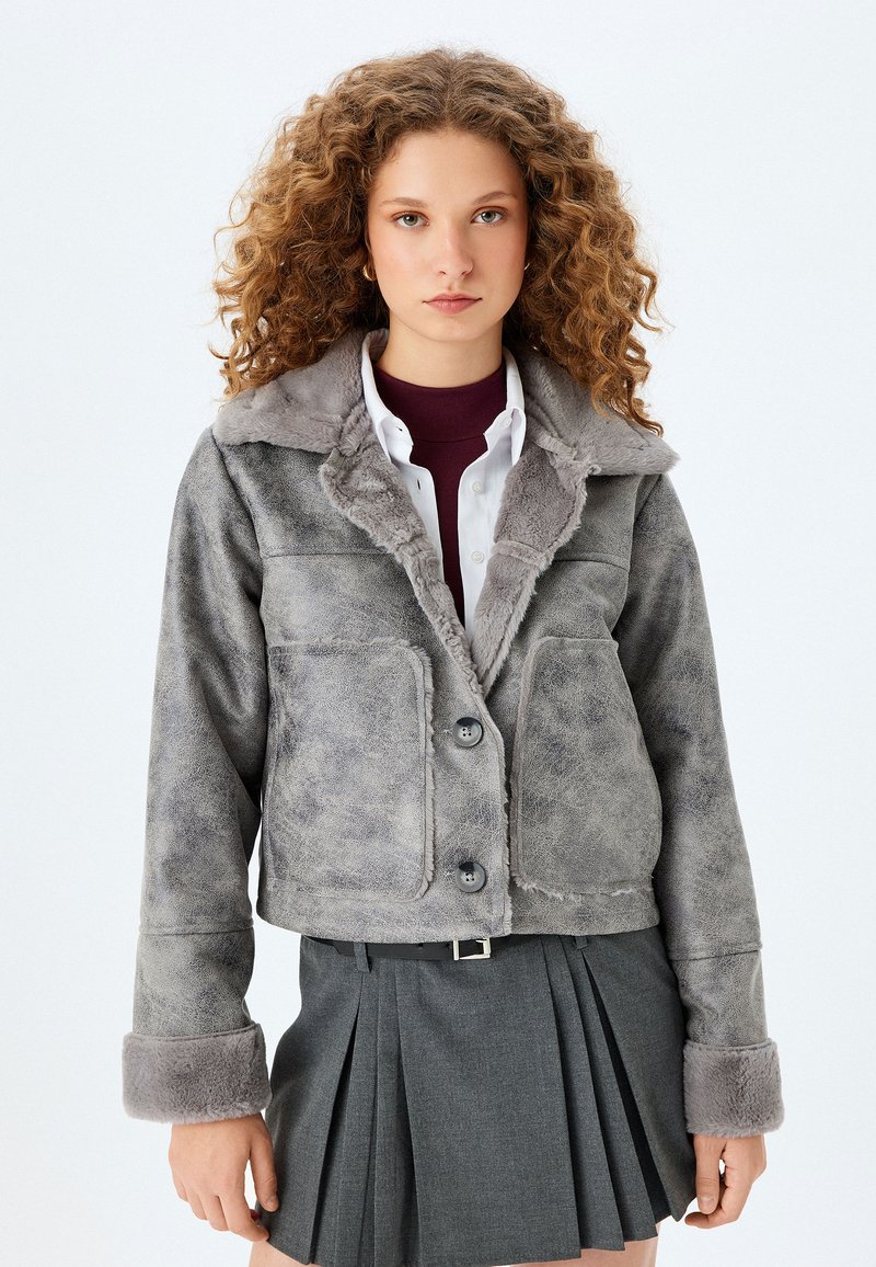 Graue, kurz geschnittene Jacke aus Kunstfell mit einem Kragen aus Kunstpelz, zwei Fronttaschen und zwei Knopfverschluss. Sie zeichnet sich durch eine weiche Textur und eine lässige Passform aus.