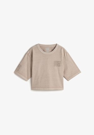 Camiseta corta beige hecha de tela suave, con mangas cortas, un escote redondo y un patrón a cuadros en el bolsillo izquierdo del pecho.