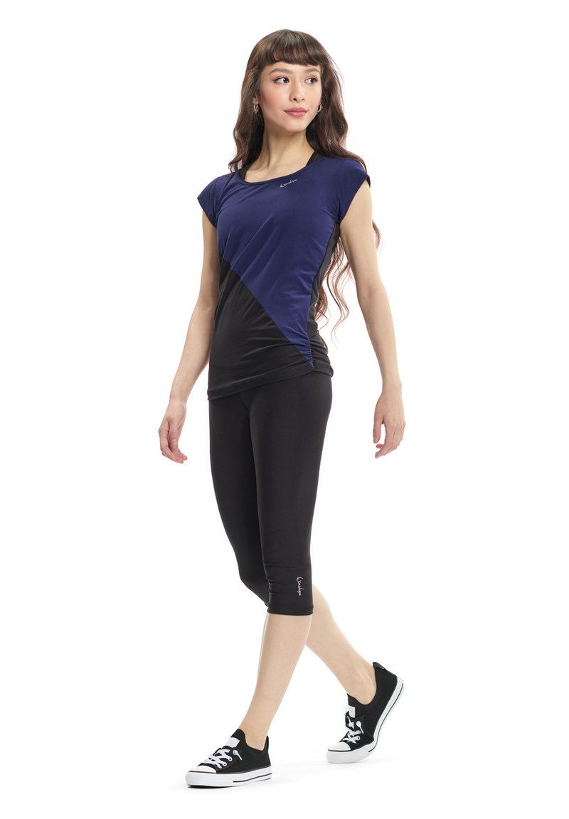 Top sportivo aderente blu navy e nero con maniche corte, design a cucitura diagonale, abbinato a leggings neri e sneakers nere. Tessuto morbido.
