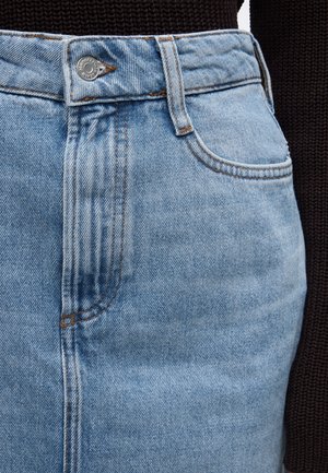 Φούστα από ανοιχτό γαλάζιο τζιν με κουμπιά μπροστά και θηλιές για ζώνη, συνδυασμένη με σκούρο πουλόβερ με υφή.