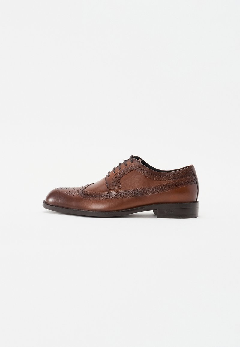 Sapato oxford em couro castanho com detalhes de brogue, atacadores fechados, bico arredondado e um salto fino. Textura suave com acabamento polido.