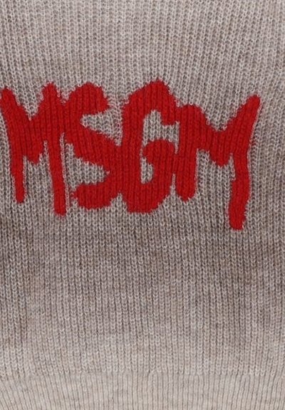 Maglione lavorato a maglia di grigio chiaro con un logo rosso prominente "MSGM" in un carattere irregolare. Il materiale sembra morbido con una leggera trama.