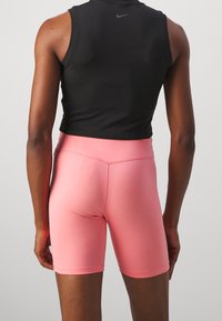 Top senza maniche nero abbinato a pantaloni shorts a vita alta rosa, che mostrano un tessuto liscio, un design aderente e una finitura pulita sui bordi.