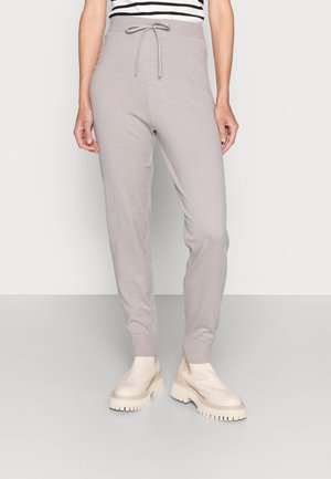 Calças de jogging de malha cinza claro com cintura elástica e punhos canelados, combinadas com botins bege com sola de borracha grossa.