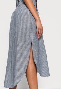 Jupe midi rayée en bleu clair et blanc, fabriquée en tissu texturé. Elle dispose d'une fente sur le côté et d'une coupe ajustée avec une taille cintrée.