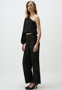 Zwart, gestructureerd two-piece outfit met een asymmetrische top met één lange mouw en wijde broekspijpen, aangevuld met zwarte hakken.