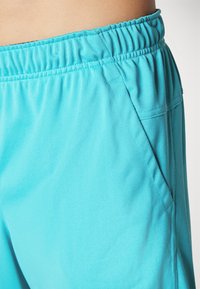 Pantalones cortos deportivos en color turquesa con cinturilla elástica, tejido texturizado y detalle de bolsillos laterales. El diseño es práctico y ligero.