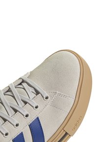 Sneaker in camoscio bianco con strisce blu, lacci bianchi e suola in gomma marrone chiaro. Presenta una parte superiore testurizzata e un accento di marca.