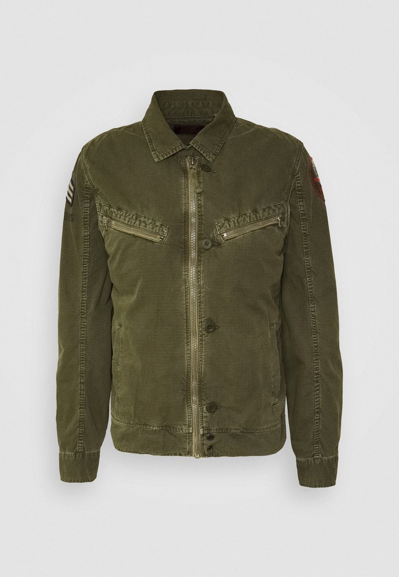 Giacca verde oliva chiaro con colletto, chiusura frontale con zip, due tasche con zip e dettagli con toppe sulle spalle. Realizzata in tessuto strutturato.