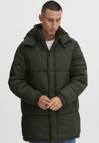 Mørkegrønn puffjakke laget av quiltet stoff. Den har glidelås foran, justerbar hette og elastiske mansjetter, og gir en uformell, oversized passform.