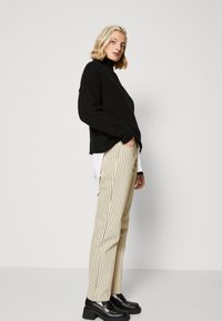 Musthave mustripp-sweater, lõdva istuvusega; koorevärvi triibulised püksid; mustad platvormi loafersid. Minimalistlik disain, keskendudes tekstuurile ja kihistamisele.