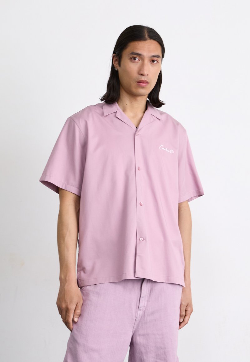 Korte mouwen, knoopsluiting shirt van lichtroze stof met een gladde textuur. Heeft een kraag en een klein wit logo op de borstzak.