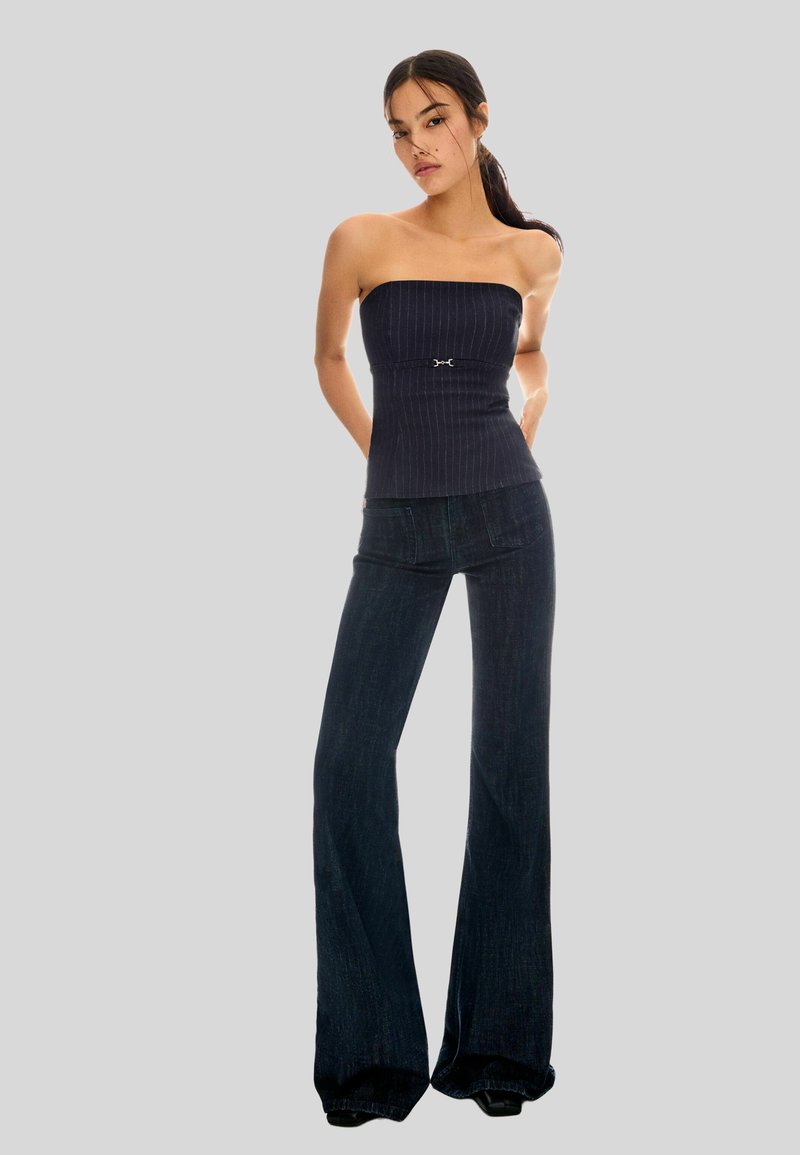 Top sans bretelles, bleu foncé à côtes avec une boucle en argent décorative à la taille, associé à un jean en denim foncé évasé.