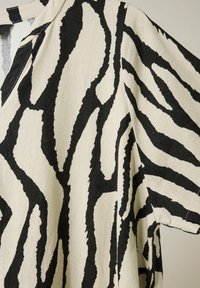 Kurzärmeliges Hemd aus strukturiertem beigem Stoff mit schwarzen Zebrastrichen, ausgestattet mit einem V-Ausschnitt und lockerer Passform.