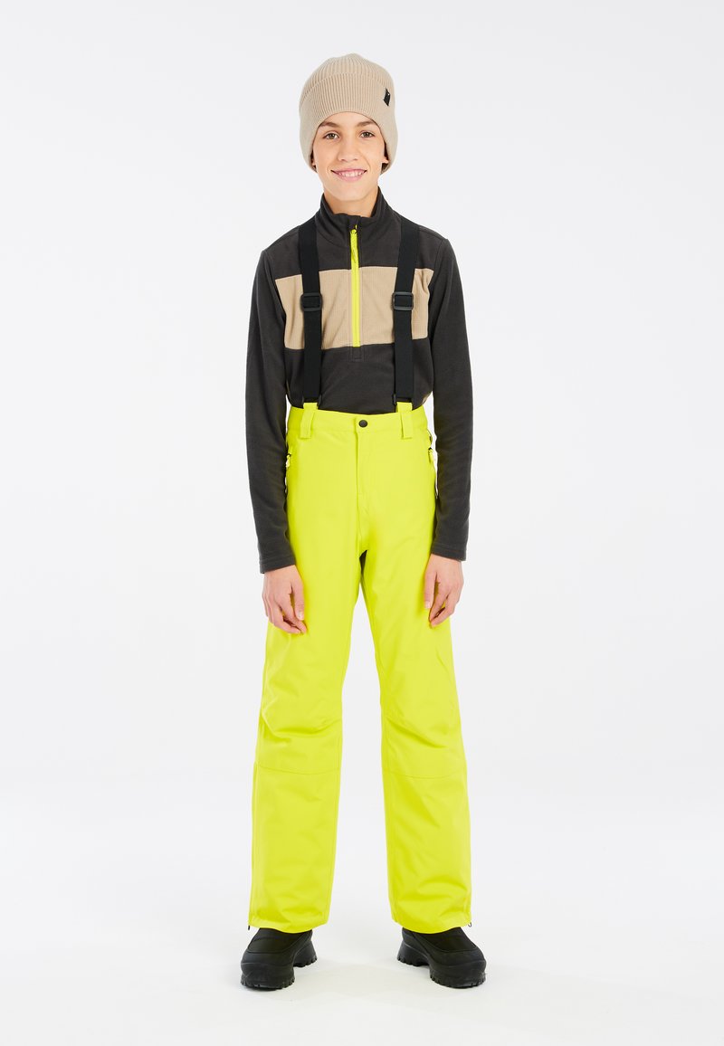 Gelbe wasserdichte Skihose, schwarzes Langarmshirt mit beigem Muster, graue Mütze und schwarze Schuhe. Verstellbare Träger inklusive.