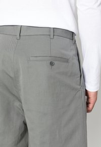 Pantaloni di cotone grigi con una trama liscia, dotati di una tasca posteriore con chiusura a bottone e passanti per cintura per una vestibilità regolabile.