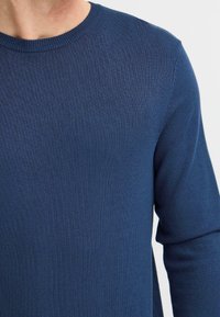 Pulover tricotat de culoare albastru marin, cu guler rotund și manșete cu nervuri, având o textură netedă și o formă ajustată, potrivit pentru o ținută casual.