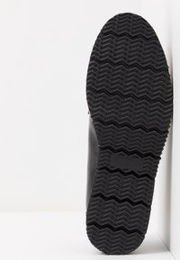 Svart gummisula med zigzag-mönster. Skons ovandel är slät med rundade kanter, med minimal detaljering och en dämpad finish.