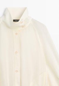 Wit overhemd met hoge kraag en zichtbare merklabel aan de binnenkant van de nek, gemaakt van gestructureerde stof.