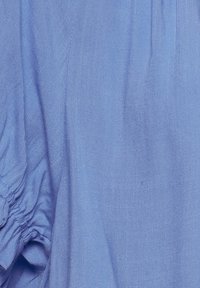 Tessuto azzurro chiaro con un motivo testurizzato e dettagli morbidi e arricciati sulle maniche. Materiale liscio e leggero.