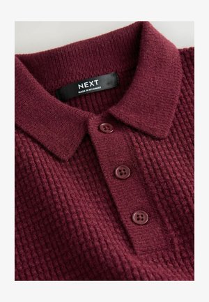 Cămașă polo tricotată de culoare burgundă, cu un model texturat și trei nasturi asortați. Eticheta menționează "NEXT, Fabricat în Myanmar."