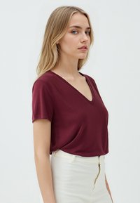 Maglietta V-neck bordeaux in tessuto morbido, maniche corte, vestibilità rilassata, abbinata a pantaloni bianchi a vita alta. Design minimalista, senza fantasie.
