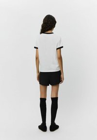Vit t-shirt med svart rundhals och ärmslut, tillsammans med svarta shorts och knähöga svarta strumpor, bärs med svarta skor.