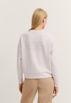 White sweatshirt with dropped shoulders, ribbed cuffs, and a large logo in lighter text on the back. Smooth, soft texture, casual fit.