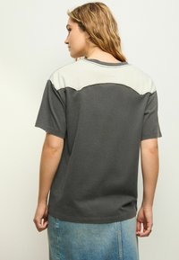 T-shirt gris avec empiècement léger gris aux épaules, manches courtes et col rond. Texture douce, coupe décontractée, associé à une jupe en denim.