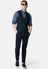 Niebiesko-granatowa kamizelka w kratę nałożona na niebieską koszulę, czarne spodnie i ciemne trampki. Dodatki to okulary przeciwsłoneczne. Dopasowany krój z zapięciem na guziki.