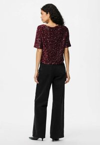 Burgundi spalvos blizgučių marškiniai su trumpomis rankovėmis, derinami su juodomis plačiomis kelnėmis ir juodais smailiais aukštakulniais. Sklandus audinys su žėrinčia tekstūra.