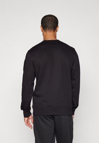 Sweat-shirt noir à col rond fabriqué en tissu doux, avec des manches longues et des poignets côtelés. Il présente un design uni, sans logos ni motifs visibles.