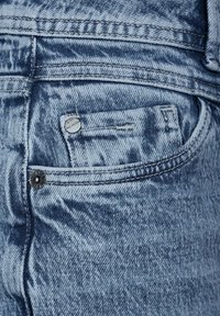 Jeans de mezclilla azul claro con un bolsillo trasero con cierre de botón, detalles de costura sutiles y una tela suave y texturizada.