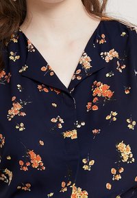 Námořnická blůza s květinovým vzorem v oranžové a žluté barvě, s výstřihem do V a krátkými rukávy. Vyrobena z lehkého materiálu.