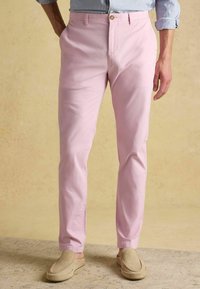 Lichtroze katoenen chinos met een ontspannen pasvorm, riemlussen, zijzakken en een sluiting met één knoop. Gecombineerd met beige instapschoenen.