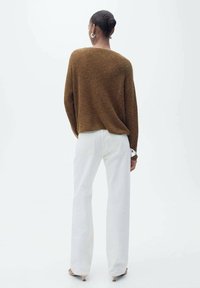 Bruine gebreide trui met een losse pasvorm, gecombineerd met witte hoogwaist rechte jeans. De look heeft een minimalistisch ontwerp.