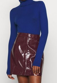 Niebieski sweter typu golf wykona z miękkiego dzianiny, zestawiony z błyszcząco bordową skórzaną mini spódnicą z guzikami z przodu i eleganckim krojem.