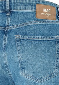 Blaue Jeans aus Denim mit texturierter Oberfläche, versehen mit einem braunen Lederetikett mit der Aufschrift "MAC vintage" und einer Gesäßtasche mit kontrastierendem Stitching.