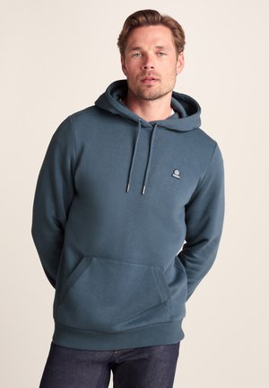 Hooded sweatshirt in deep teal, made of soft fabric with a kangaroo pocket. Features drawstrings and a small logo on the chest.