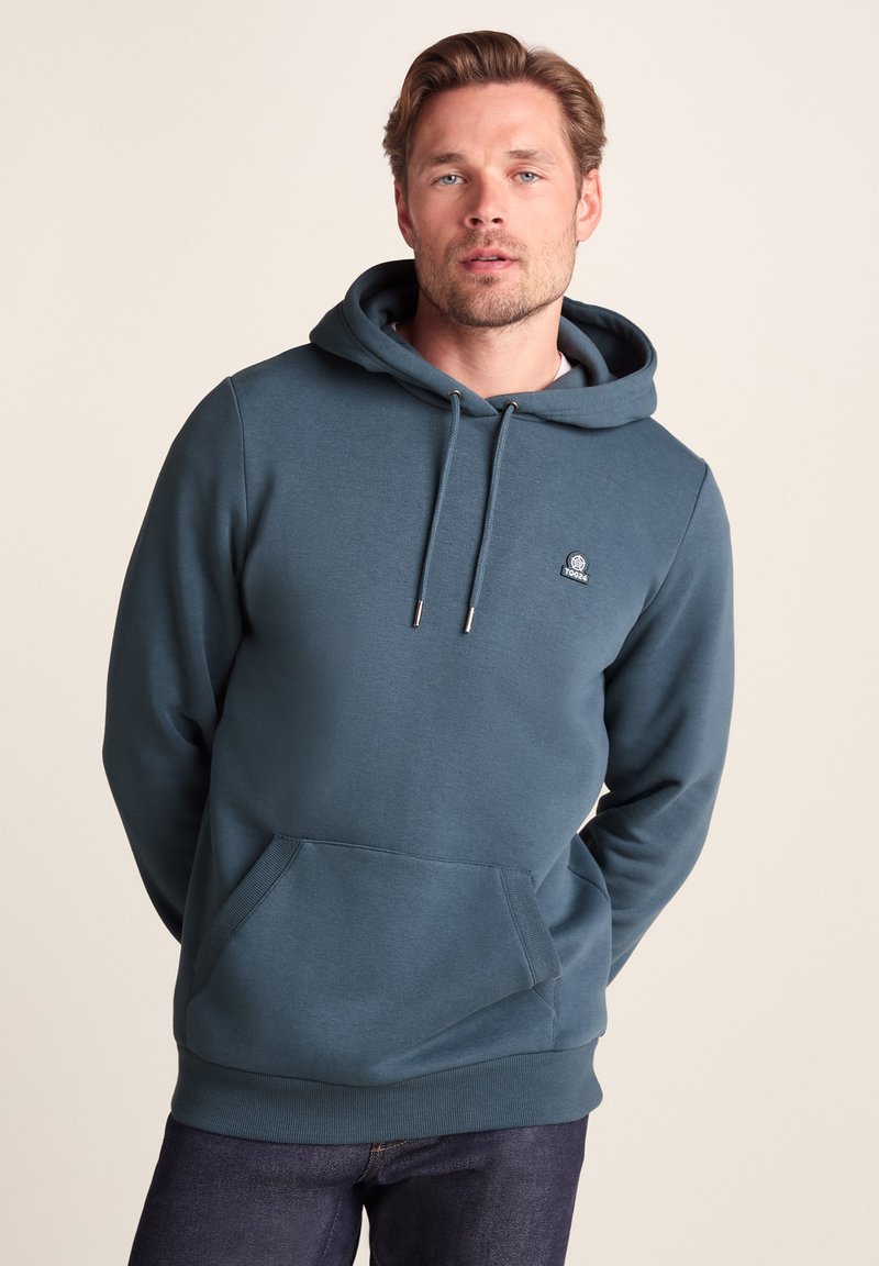 Hooded sweatshirt in deep teal, made of soft fabric with a kangaroo pocket. Features drawstrings and a small logo on the chest.